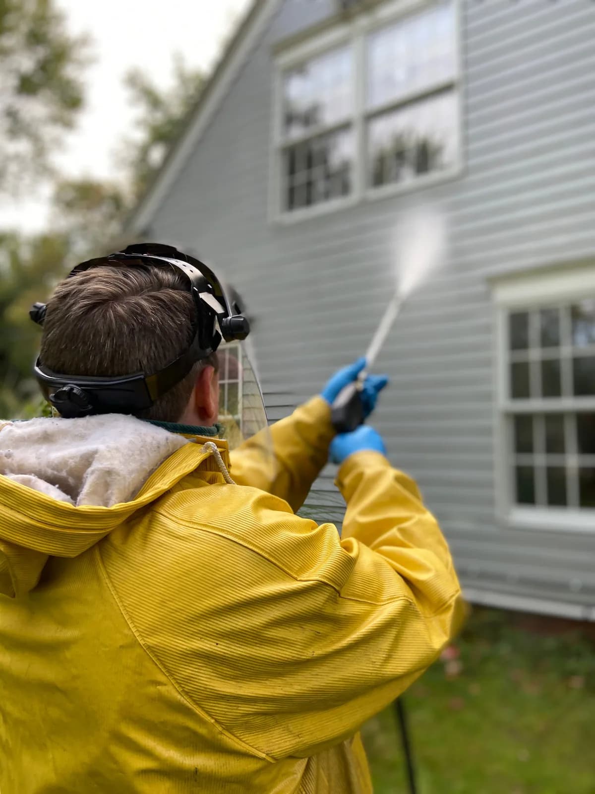 Worker in protective gear pressure-washing a building facade