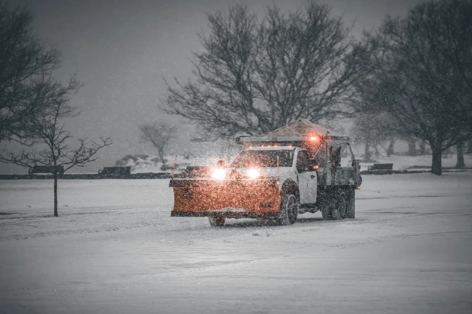 Snow plough truck clearing a parking area during heavy snowfall